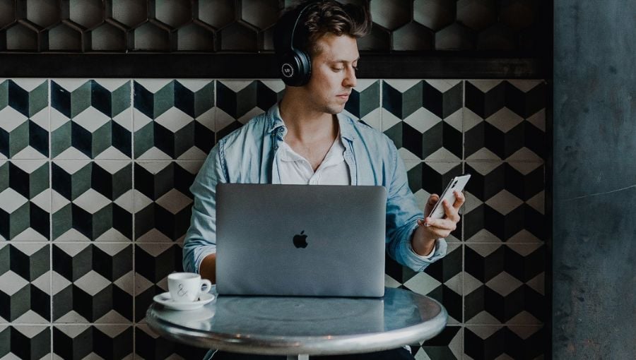 Developer working on a macbook and phone on new Ziflow product updates in March by cafe table